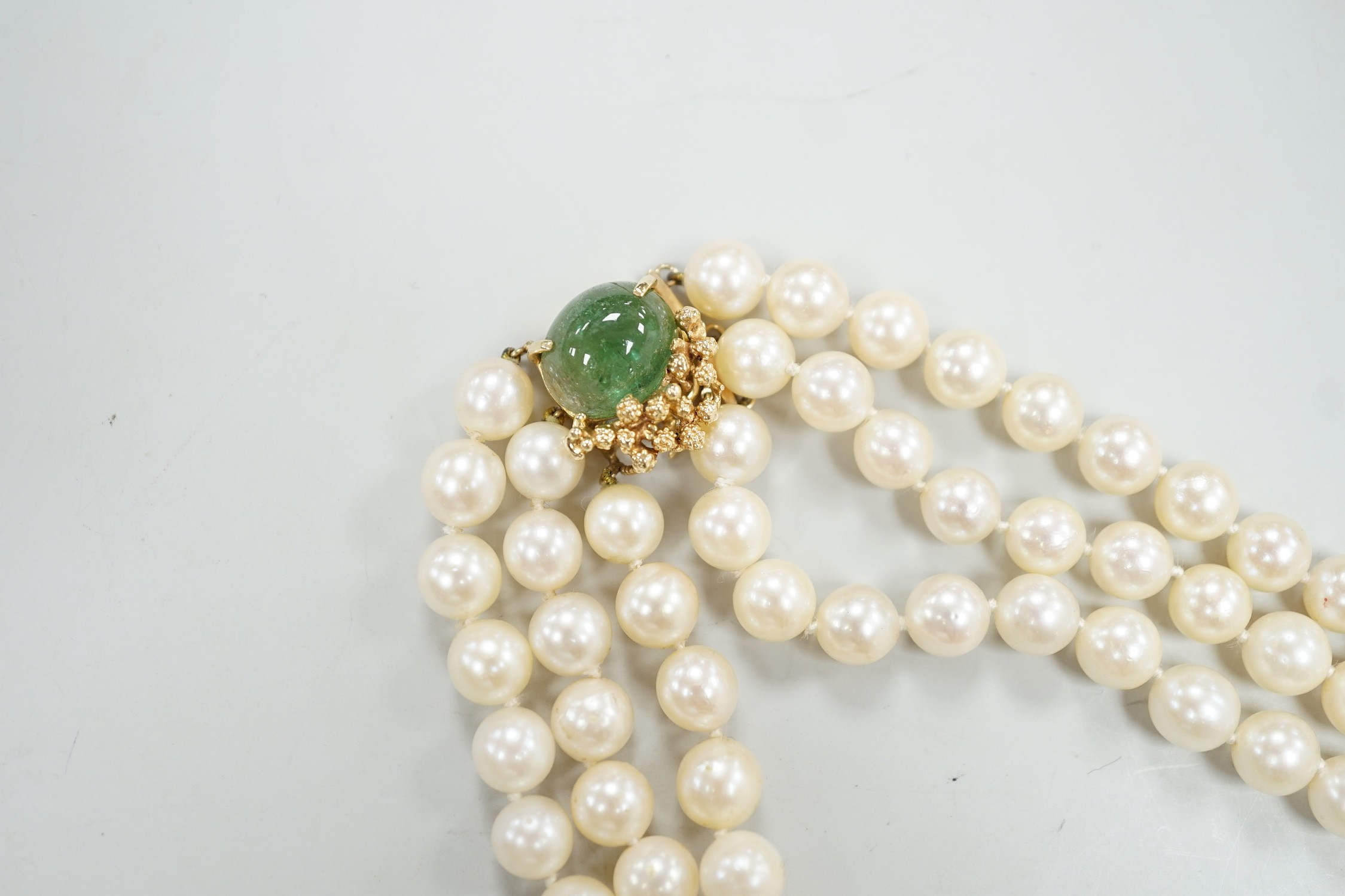 A mid to late 29th century triple strand cultured pearl choker necklace, with 14k and cabochon emerald set clasp, 34cm.